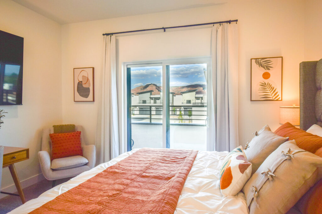 Primary bedroom with armchair and balcony view of red rock